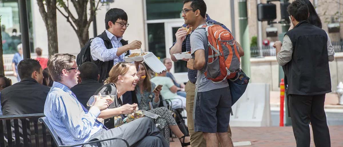 students and professors gathered around a bench eating lunch and talking together