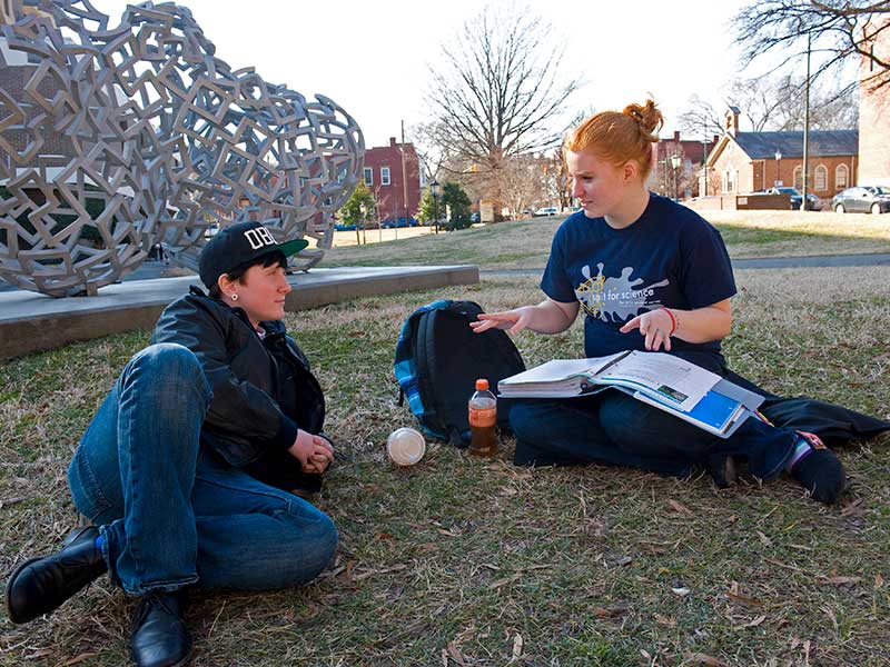 two students studying on the grass in front of an abstract sculpture